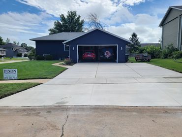 Newly poured concrete driveway leading to a blue house with garage cars.
