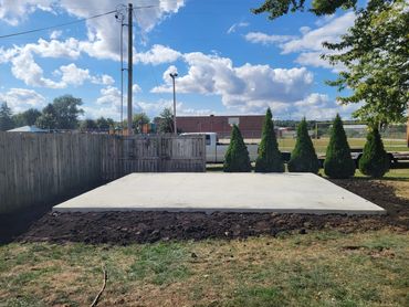 Freshly poured concrete slab in a backyard under a bright blue sky.