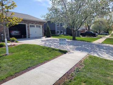 Newly poured concrete driveway in a suburban neighborhood with a Dixon Concrete sign.