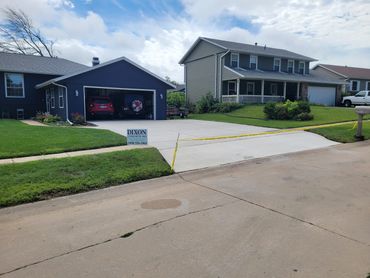 Newly poured concrete driveway with caution tape in front of a house.