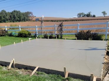 Freshly poured concrete slab set in a grassy backyard with a white fence.