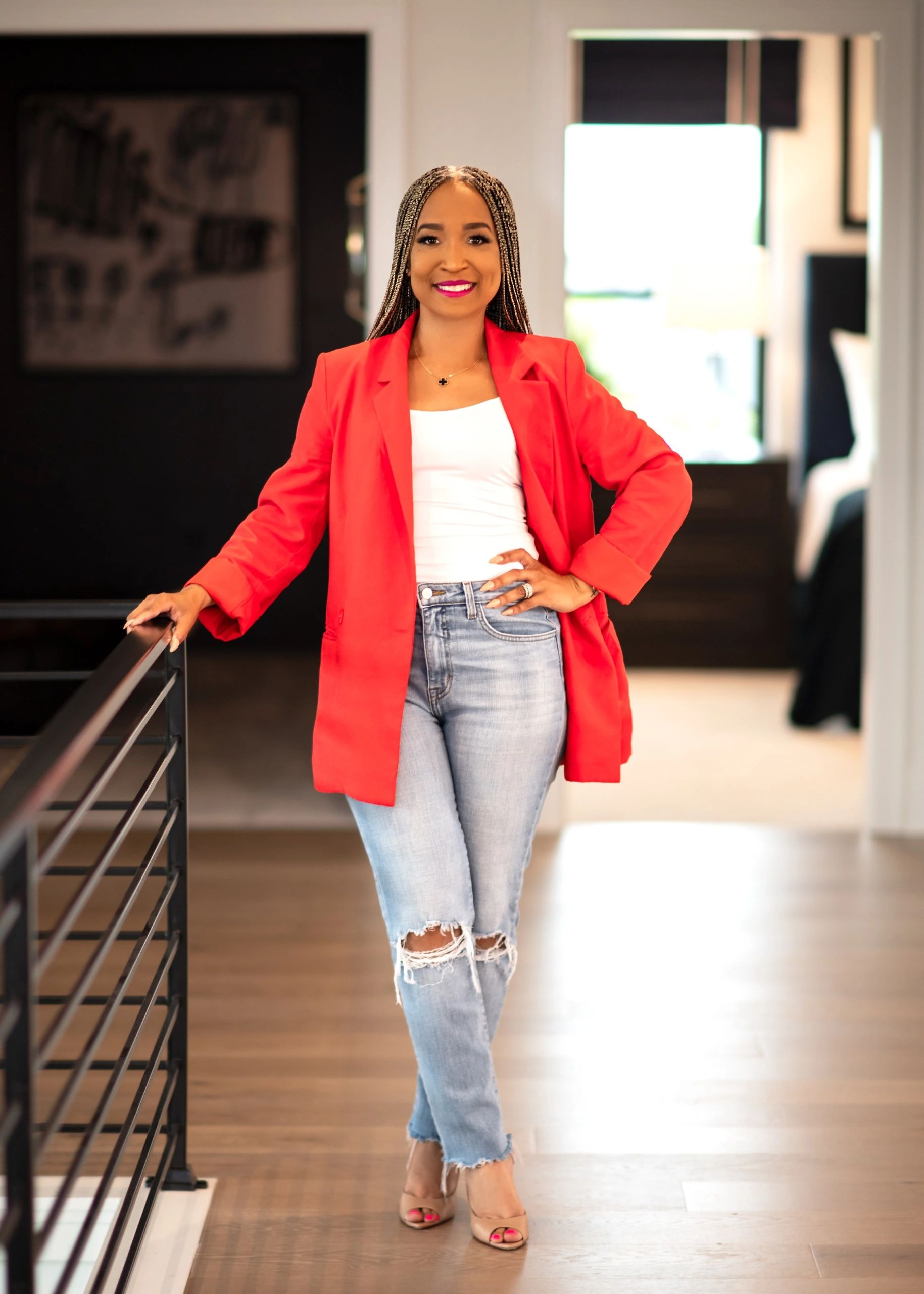 Confident woman in a red blazer and ripped jeans standing indoors.
