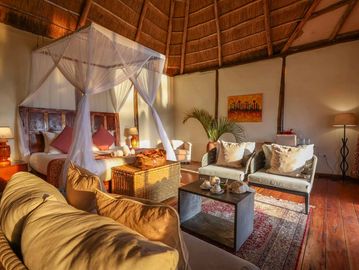 Cozy bedroom with canopy bed and comfortable seating under a thatched roof.