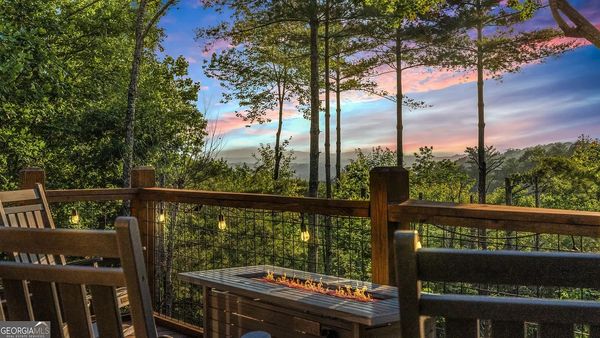 Cozy deck with fire pit overlooking a lush forest at sunset.