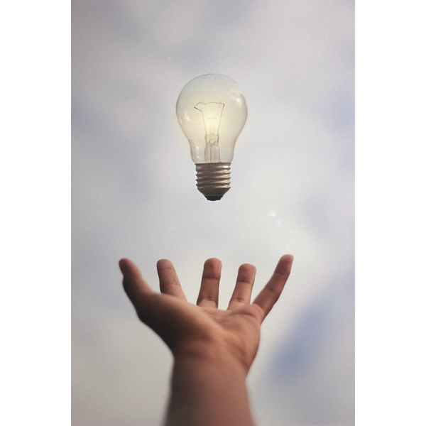 Een hand met daarboven een gloeilamp als tegen een grijze lucht als metafoor voor oplossingen