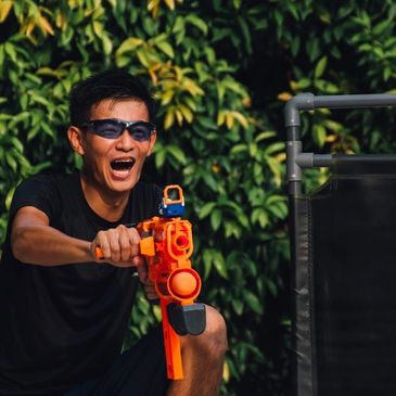 Young man joyfully playing with an orange toy gun outdoors.