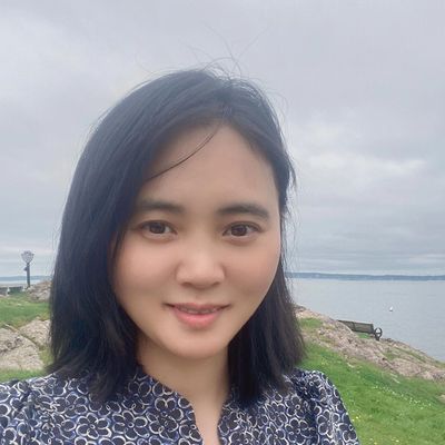 Young woman smiling outdoors near a waterfront on a cloudy day.
