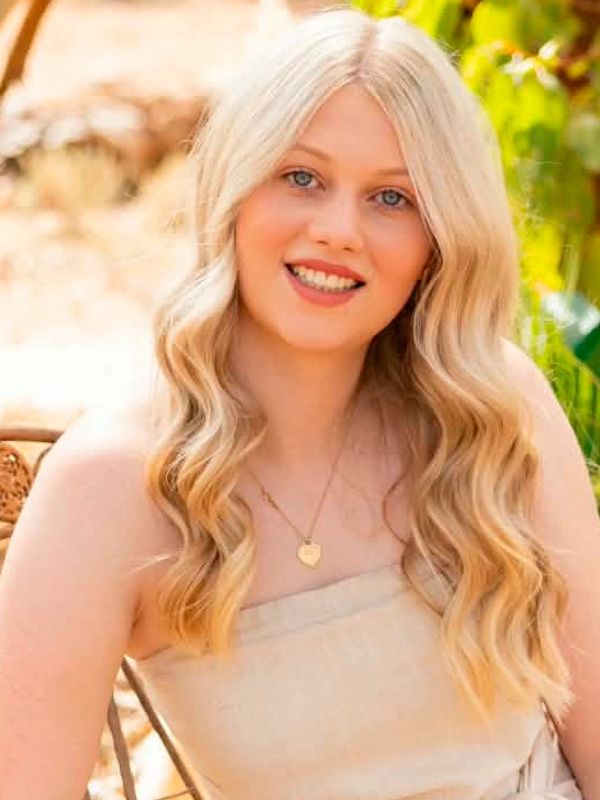 Blonde woman with wavy hair smiling outdoors.