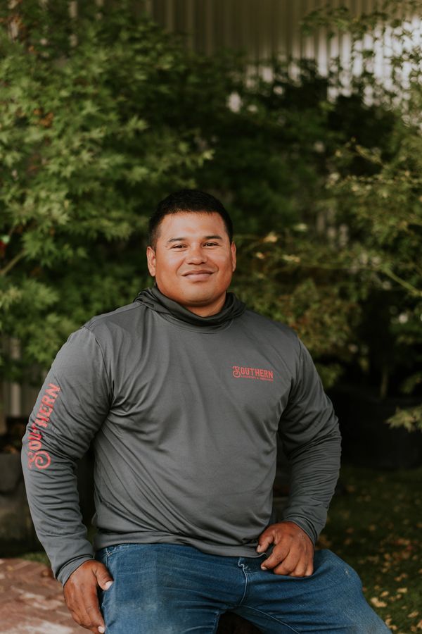 Man in a gray hoodie and jeans sitting outdoors with a smile.