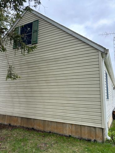 Side view of a house with beige siding and green shutters on the window.