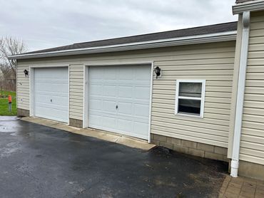 Double garage doors on a beige house with wet driveway and cloudy sky.