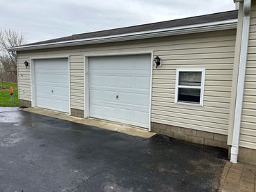 Two white garage doors on a beige house under a cloudy sky.