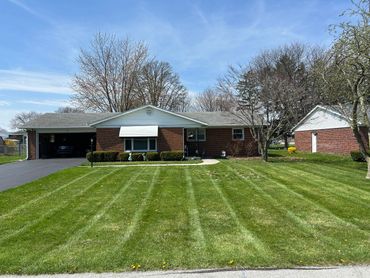 Single-story brick house with well-maintained lawn and clear blue sky.