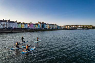 People paddleboarding near colorful houses by the water.