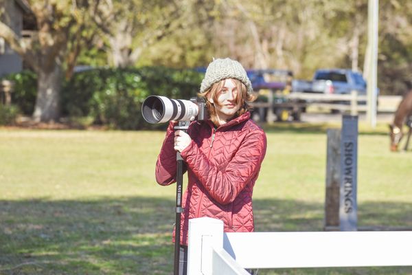 Woman in red jacket using a large camera lens outdoors.