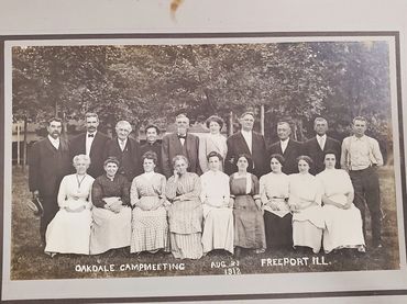 Portrait of a group of 19 people with handlettered caption at the bottom. Oakdale Campmeeting, Augus