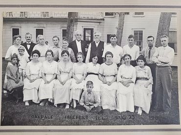 Portrait of 20 adults and 2 children standing in front of the lodge. A handwritten caption at the bo