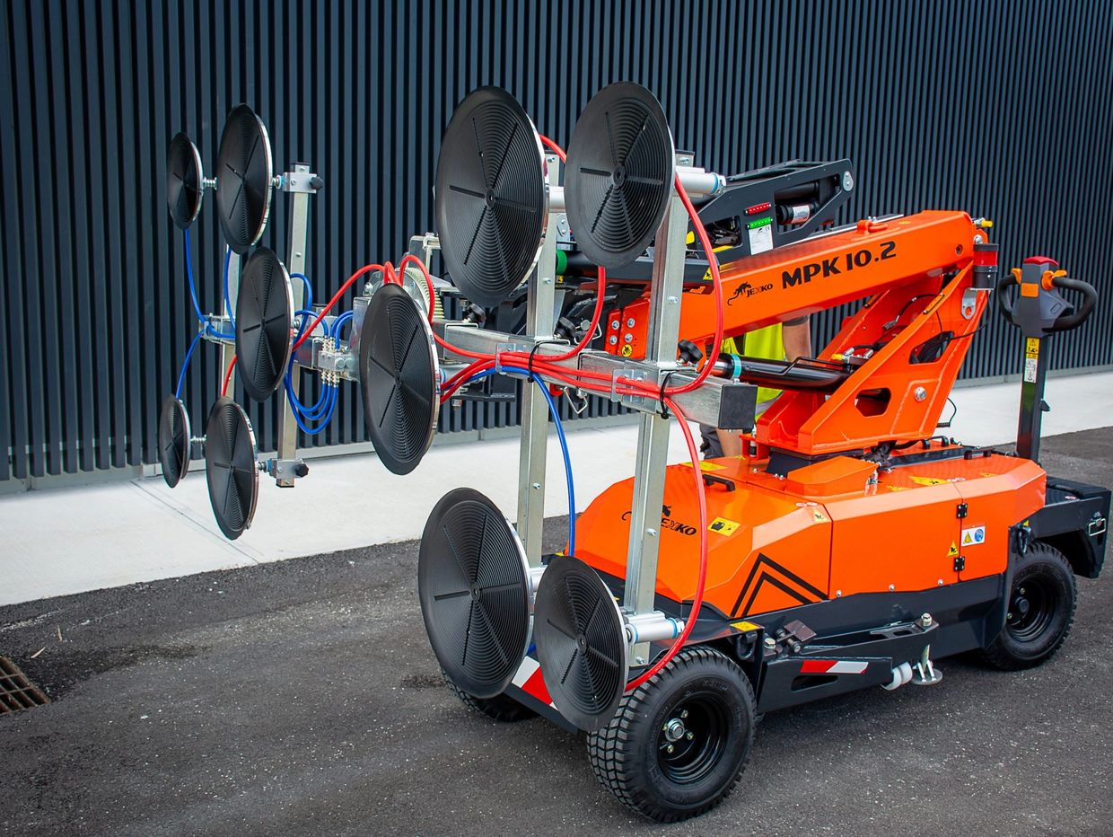Orange glass handling machine with suction pads and hydraulic arm outdoors.