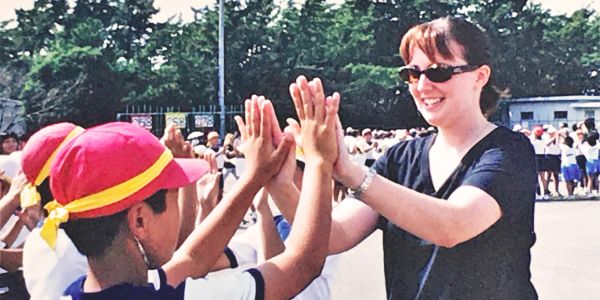 A woman and child give high fives outdoors in a sunny setting.