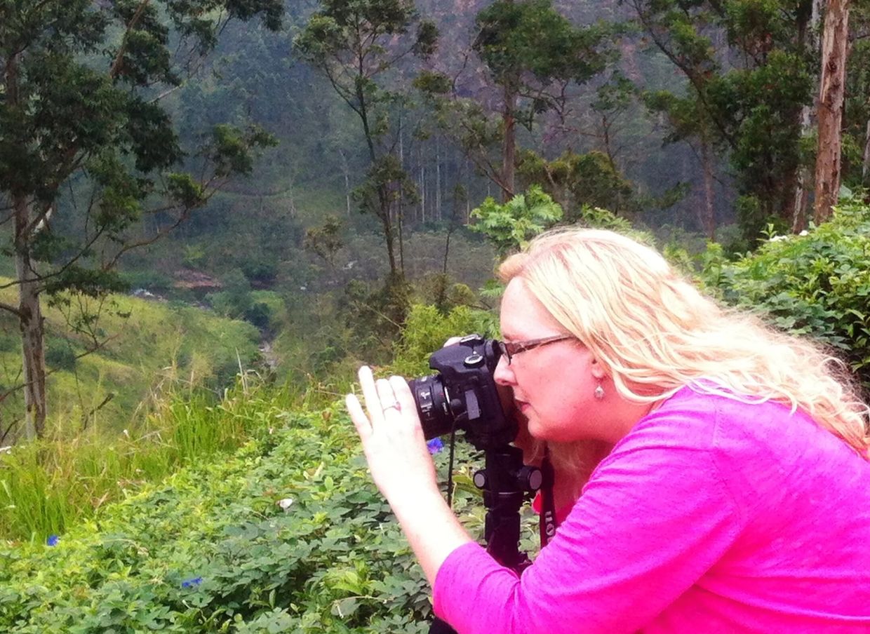 Woman in pink jacket photographing nature with a DSLR camera outdoors.