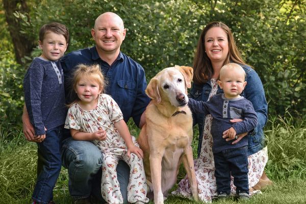 A happy family with three kids and a dog posing outdoors.
