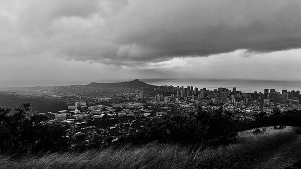 Black and white cityscape under dramatic cloudy sky with a mountain in the background.