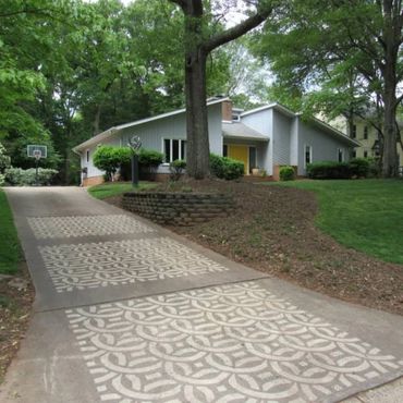 Driveway with decorative patterned concrete leading to a modern house surrounded by trees.