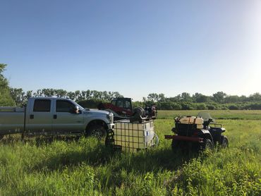 Pickup truck, ATV, and equipment in a green field under a clear sky.