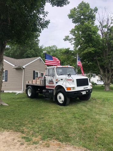 White flatbed truck with American flags parked on grass near a house.