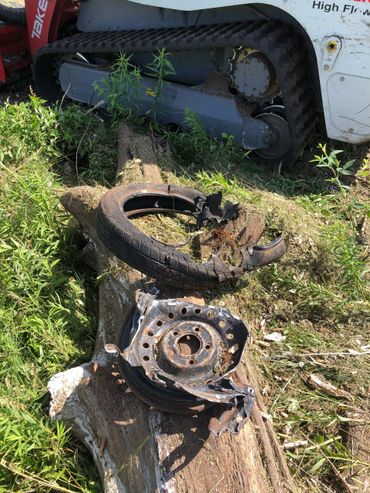 A destroyed tire and rim lie on a log near a tracked vehicle.