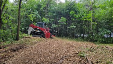 A red bulldozer clearing wood chips on a forested hill.
