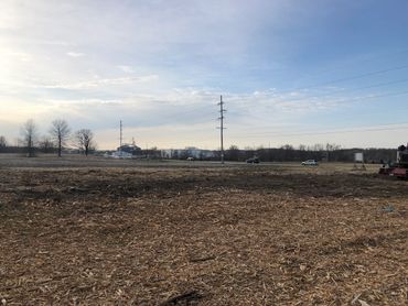 A cleared field with some vehicles and power lines under a partly cloudy sky.