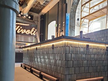 Industrial-style bar counter with tiled base and illuminated trim inside a spacious venue.