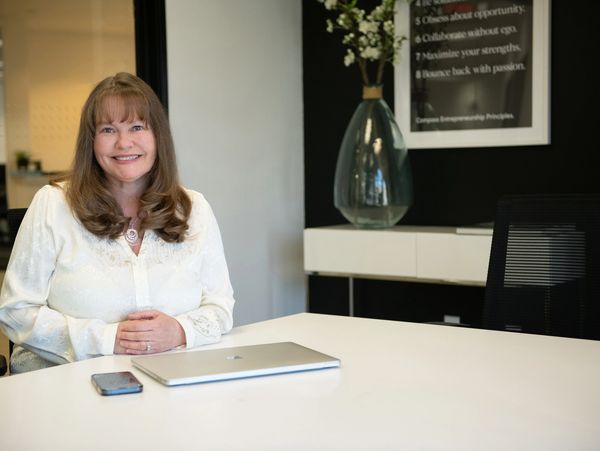 Lisa Hopkins-Cochran, Realtor®, smiling and sitting at a desk with a laptop and phone in a modern office. Providing the best real estate service for home sellers and buyers for 35 years.