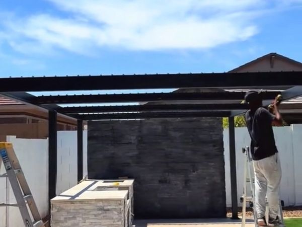 Man building a pergola over an outdoor kitchen in a backyard.