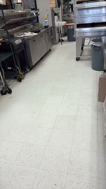 Clean commercial kitchen floor with stainless steel appliances and cleaning supplies.
