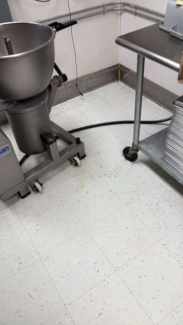 Commercial kitchen equipment on a tiled floor with some stains and a black hose.