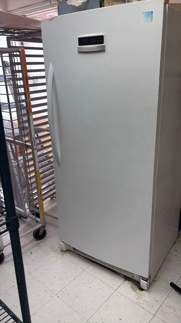 White upright freezer with digital control panel in a storage area.