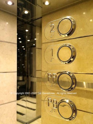 Reflejo de la cabina de un elevador de mármol y acero dorado en el panel de control