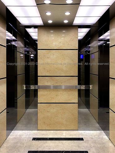 Vista frontal de un elevador con paredes de mármol y acero inoxidable acabado espejo dorado
