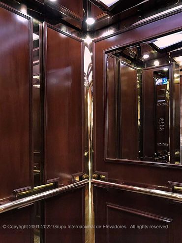 Vista a 45 grados de un elevador para pasajeros de madera natural y acero dorado