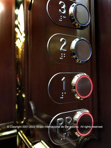 Detalle de los botones del panel de control de un elevador de madera natural y acero espejo