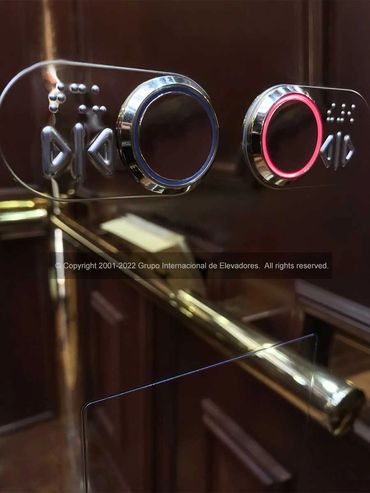 Detalle de los botones para abrir y cerrar puertas de un elevador de madera natural y acero espejo