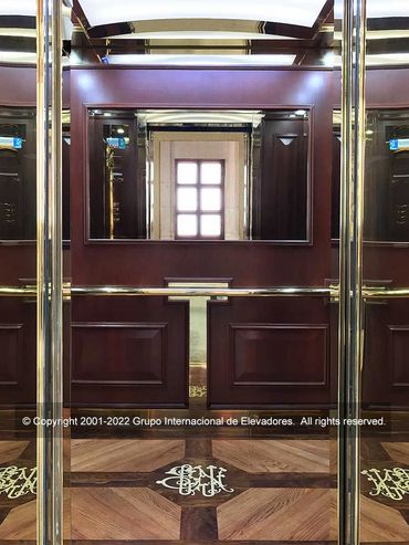 Vista frontal de un elevador para pasajeros con acabados de madera natural y acero inoxodable dorado