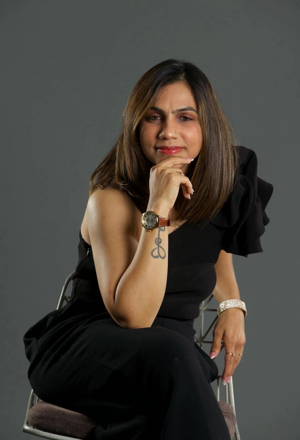 Woman posing confidently in black outfit with watch and tattoo.