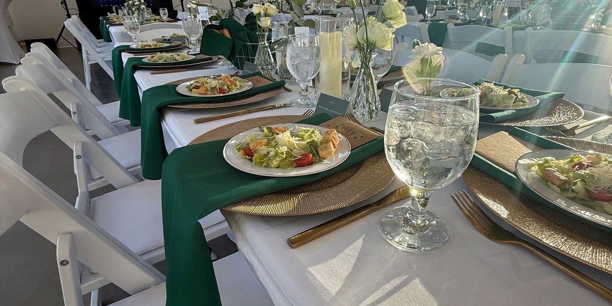 Elegant dining setup with white chairs, green napkins, salads, and water glasses.