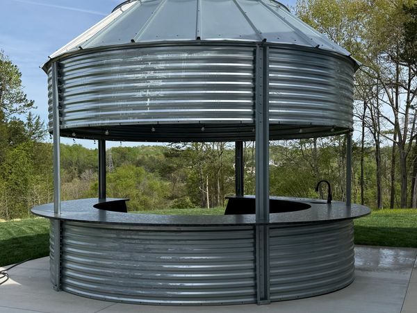 A circular outdoor metal bar with a roof in a green landscape.