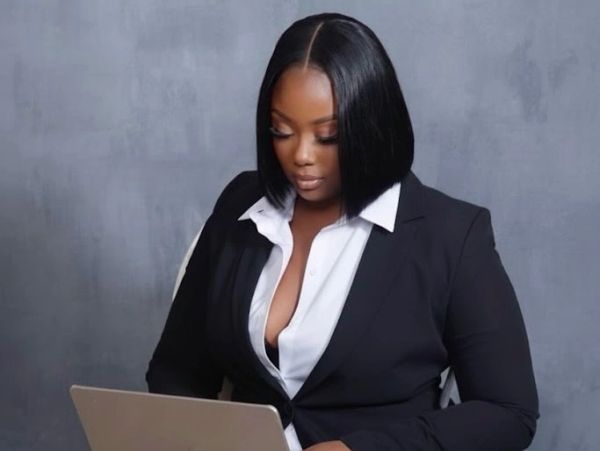 Woman in black blazer working on a laptop.