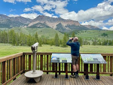 A man looking through binoculars at mountains.