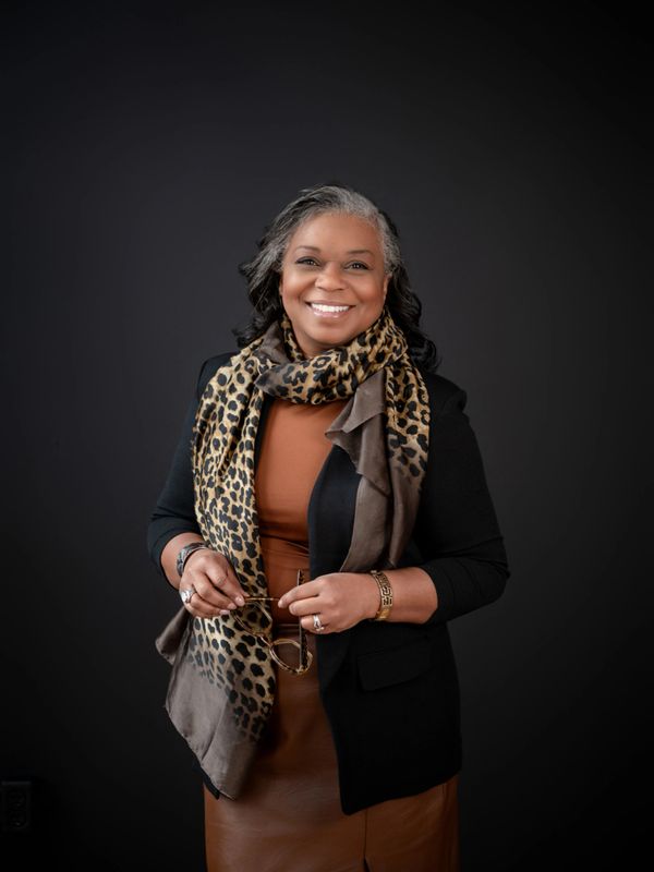 Confident woman smiling, wearing a leopard print scarf and black blazer.